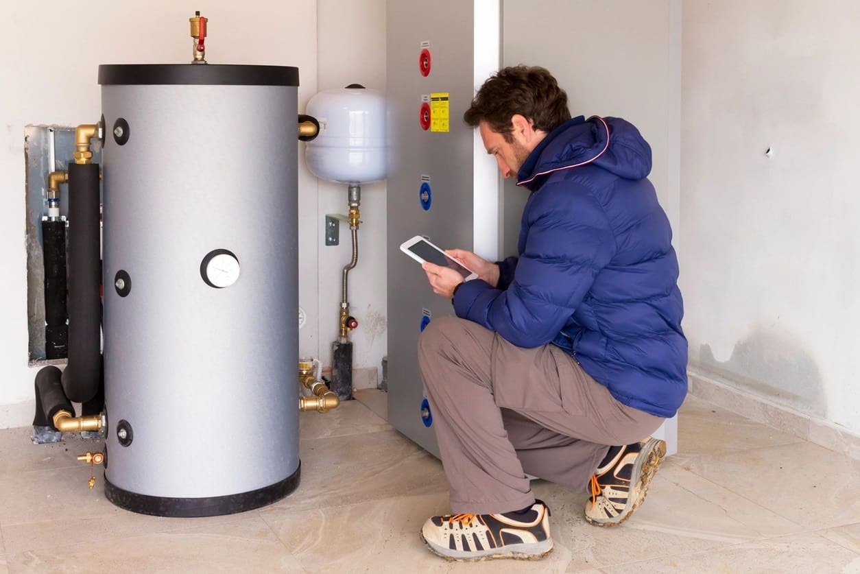 A man sitting on the floor next to an electric water heater.